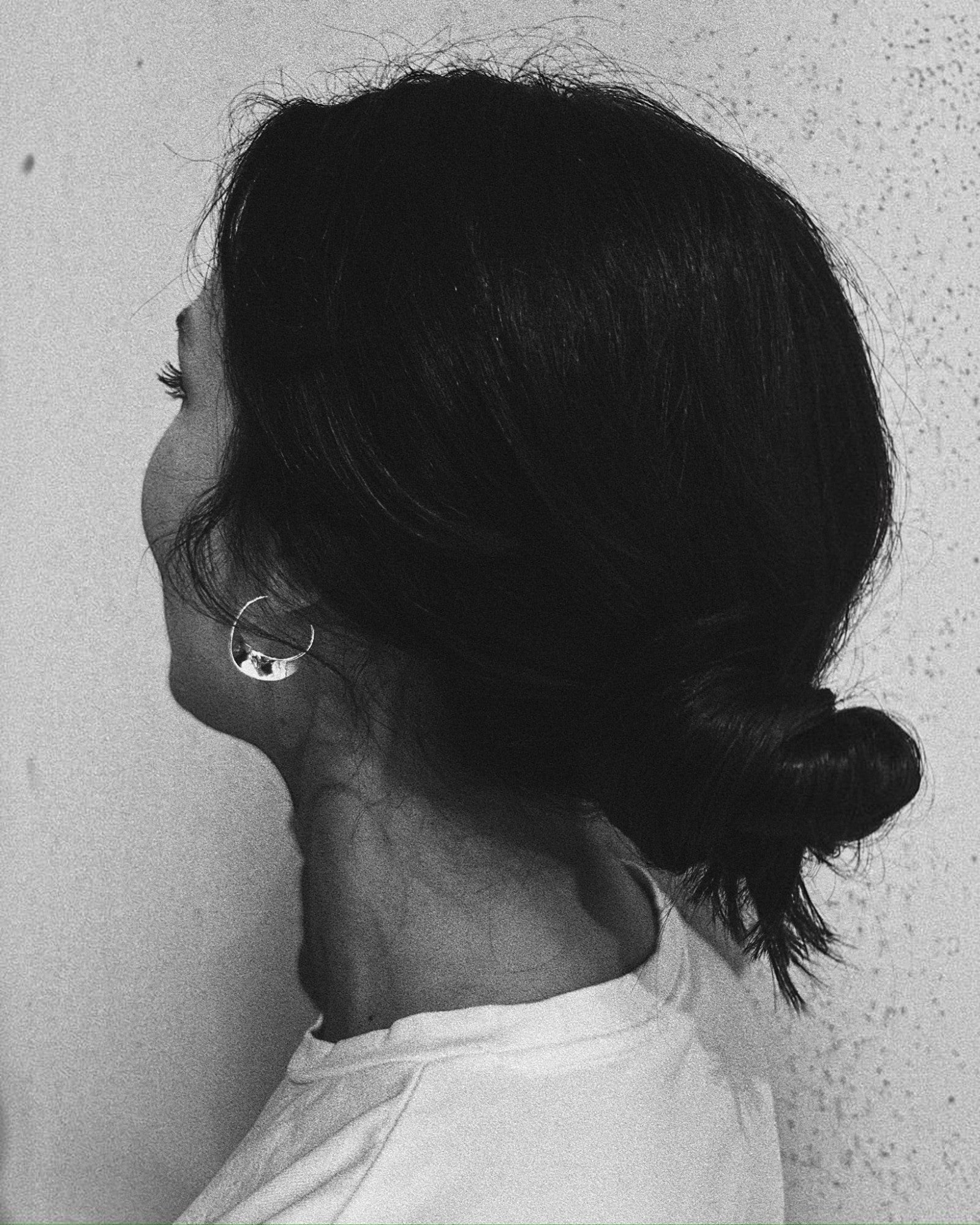Molokai Zora twisted silver hoop earring worn by a woman with hair in a bun, side profile view
